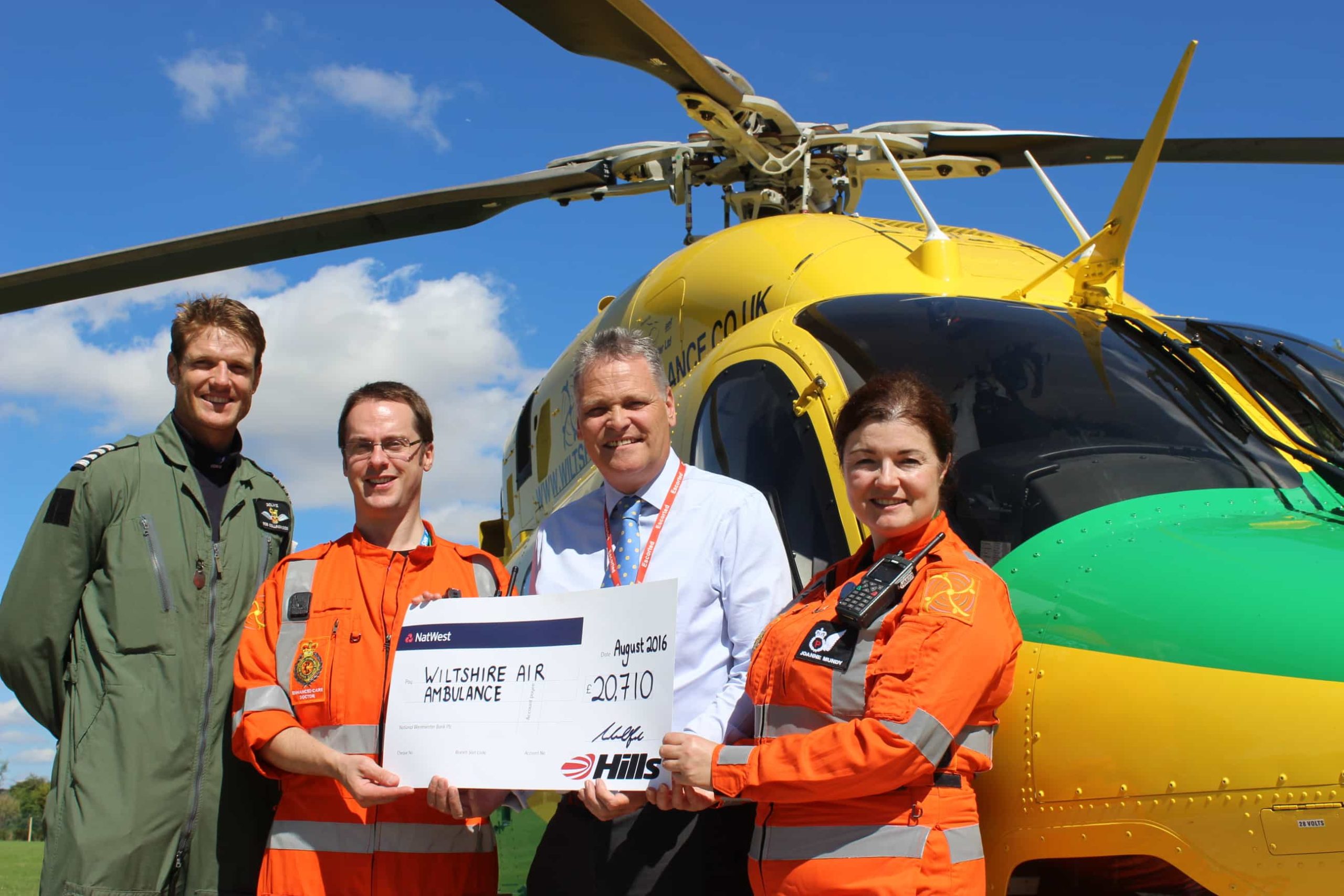 ‘Steve Burns from Hills Waste Solutions hands over a £20,710 cheque to pilot Rob Collingwood, doctor Gordon Macfarlane and critical care paramedic Joanne Munday of the Wiltshire Air Ambulance’.